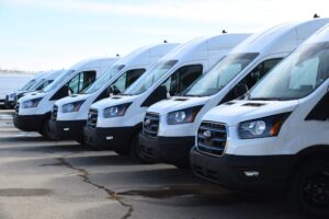 A line of Ford Transit cargo vans on a cement parking lot.