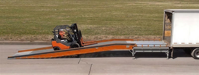 forklift driving a load up a yard ramp with a portable loading dock level off